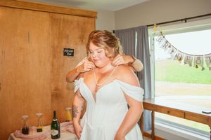 A bride gets her final dress adjustments in an off-shoulder white wedding gown.