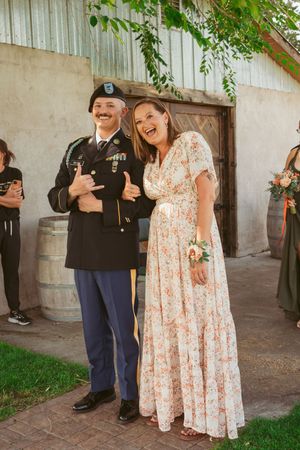 Wedding party members posing outdoors near a rustic building with greenery.