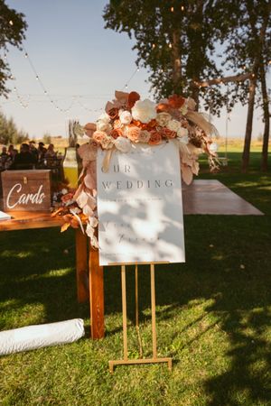 Elegant wedding signage decorated with peach flowers and string lights in an outdoor setting.