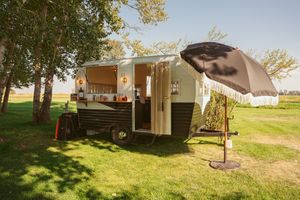 Rustic outdoor venue with mobile homes and trees against blue sky.