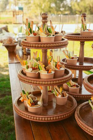 Tiered wooden display stands featuring individual appetizer cups at an outdoor wedding reception.