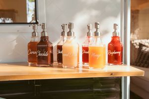 Glass bottles filled with colorful signature cocktails displayed on a wooden shelf.