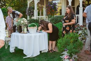 Wedding guests gather around a white-clothed signing table in a garden setting with floral decorations.