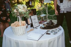 A wedding guest book table with a white tablecloth, decorated with a flower basket, sign, and chocolate dessert platter.