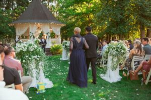 Outdoor garden wedding ceremony with guests seated on white chairs surrounded by lush greenery during golden hour.
