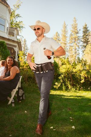 Person in cowboy hat and western attire walks on lawn with trees during golden hour sunset lighting.
