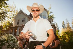 Person in a cowboy hat holds a coffee mug outdoors during golden hour sunlight.