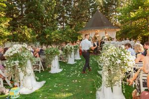 Outdoor garden wedding ceremony setup with white floral arrangements lining the aisle and guests seated on both sides.