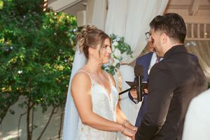 A romantic moment between bride and groom embraces in a garden setting with white floral decor and greenery.