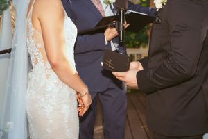 Newlyweds hold hands during an intimate outdoor wedding ceremony with floral decorations and classical attire.