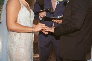 A couple exchanges wedding rings during intimate ceremony with officiant holding ceremony book between them.