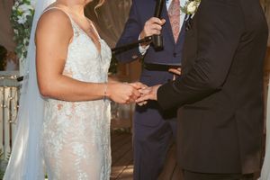Bride and officiant stand together during outdoor wedding ceremony wearing formal attire.