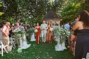 Wedding guests gather outdoors on a grassy lawn at sunset during a summer garden celebration.