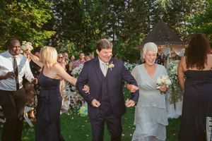 Wedding guests celebrate and dance together on a green lawn during an outdoor garden reception ceremony.
