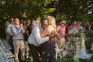 Guests gather outdoors at a garden party under lush greenery while enjoying drinks and conversation on a summer evening.
