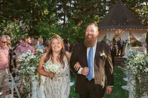 Two people share a joyful moment walking down an outdoor garden path at a wedding reception with a gazebo in the background.