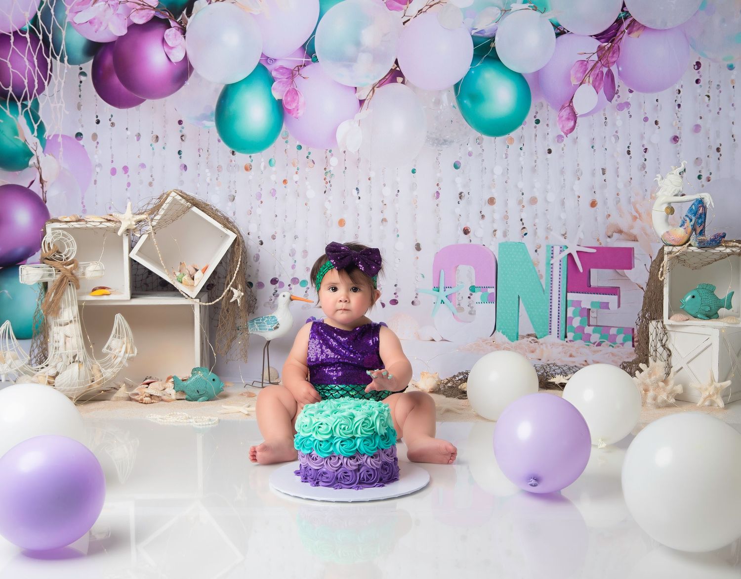 First birthday cake smash setup with purple and teal balloon arch and decorations.