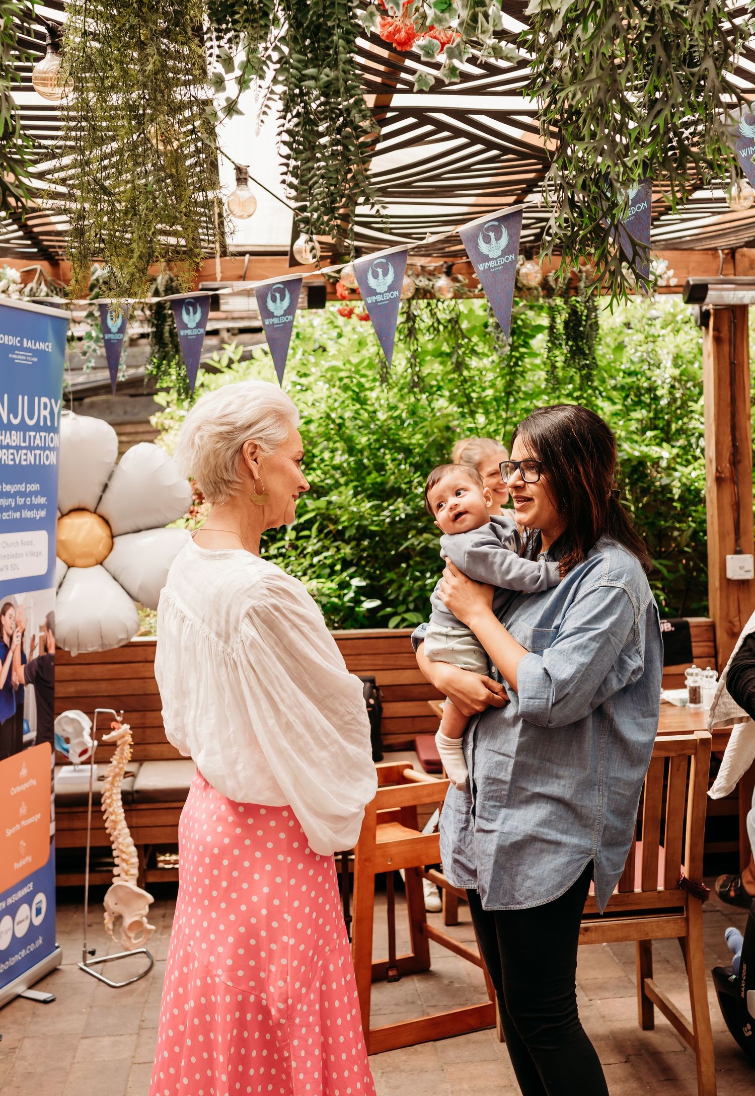 Three people having a cheerful conversation under decorative bunting at an outdoor patio setting.