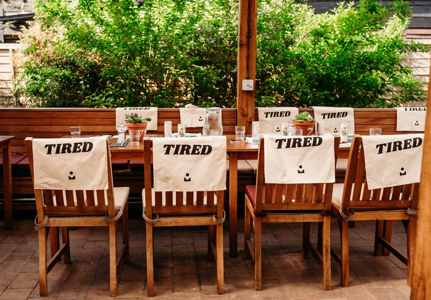 Row of wooden dining chairs with 'TIRED' signs displayed on their backs in an outdoor restaurant setting.