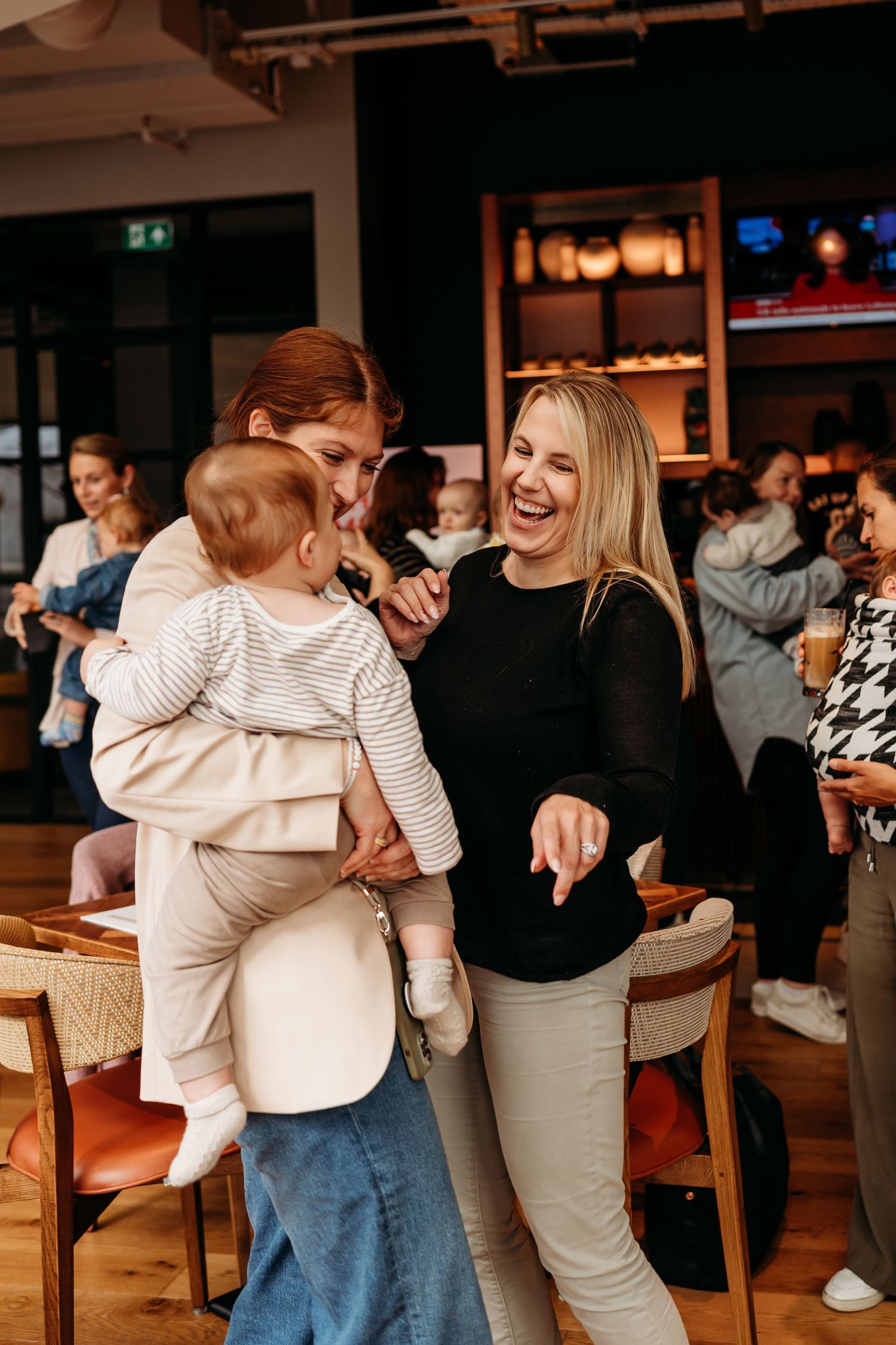 Three people share a joyful moment together in a restaurant with wooden floors and warm lighting.