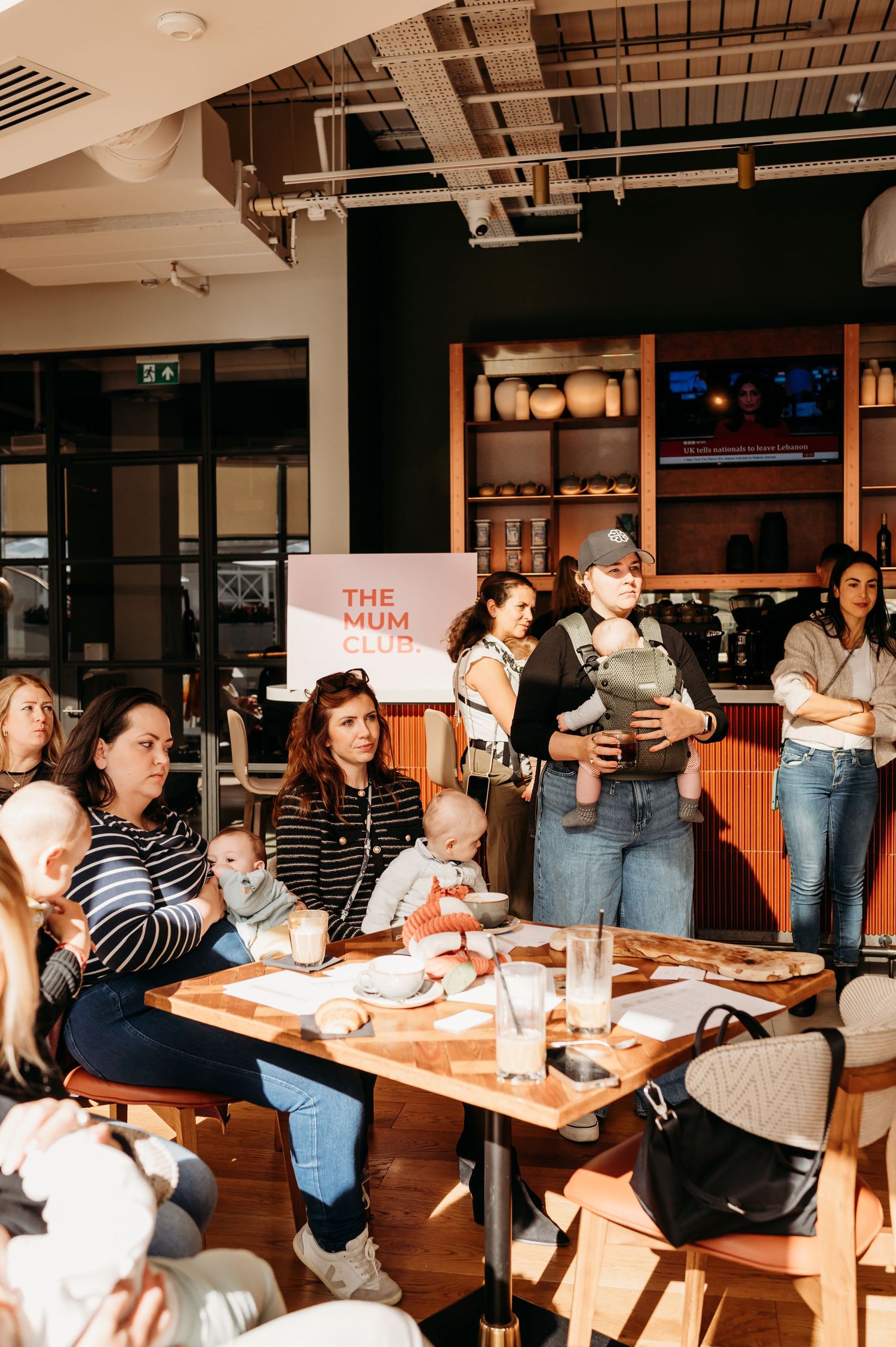 Group of parents and young children gathered around a table at a casual restaurant with exposed industrial ceiling.