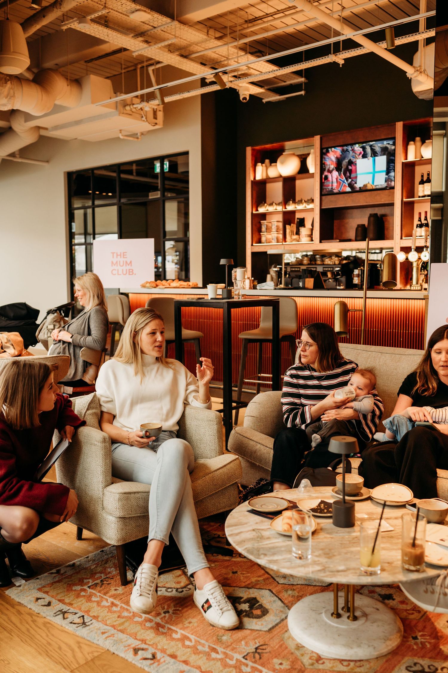 A group of friends enjoying drinks and conversation in a modern lounge space with wood accents and rustic decor.