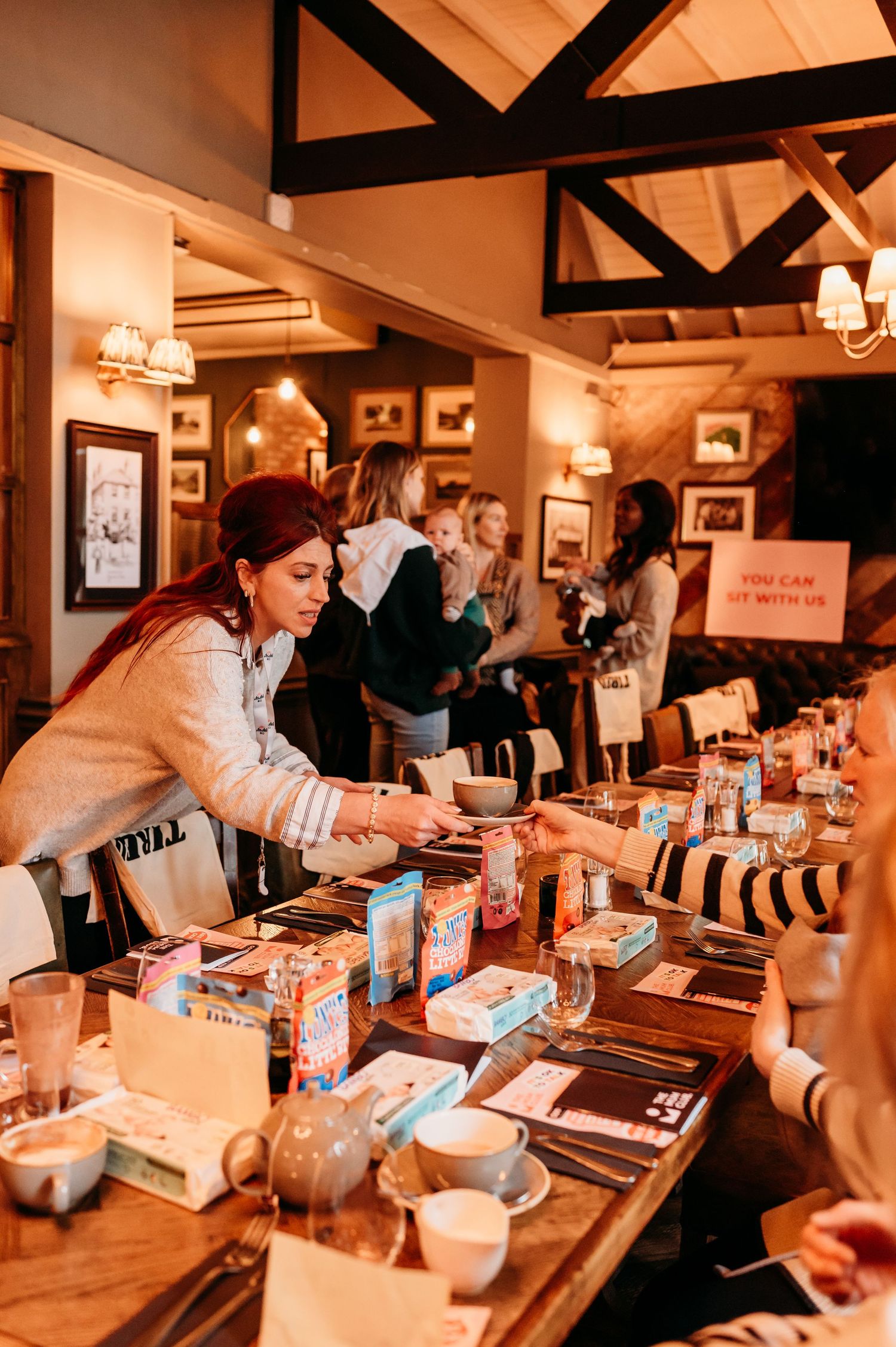 People gathered around a rustic wooden dining table in a cozy restaurant with warm lighting and exposed beams overhead.