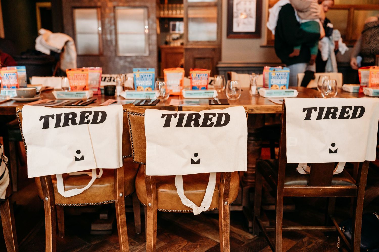 Three chairs with 'TIRED' signs hanging on their backs at a wooden dining table in a restaurant setting.