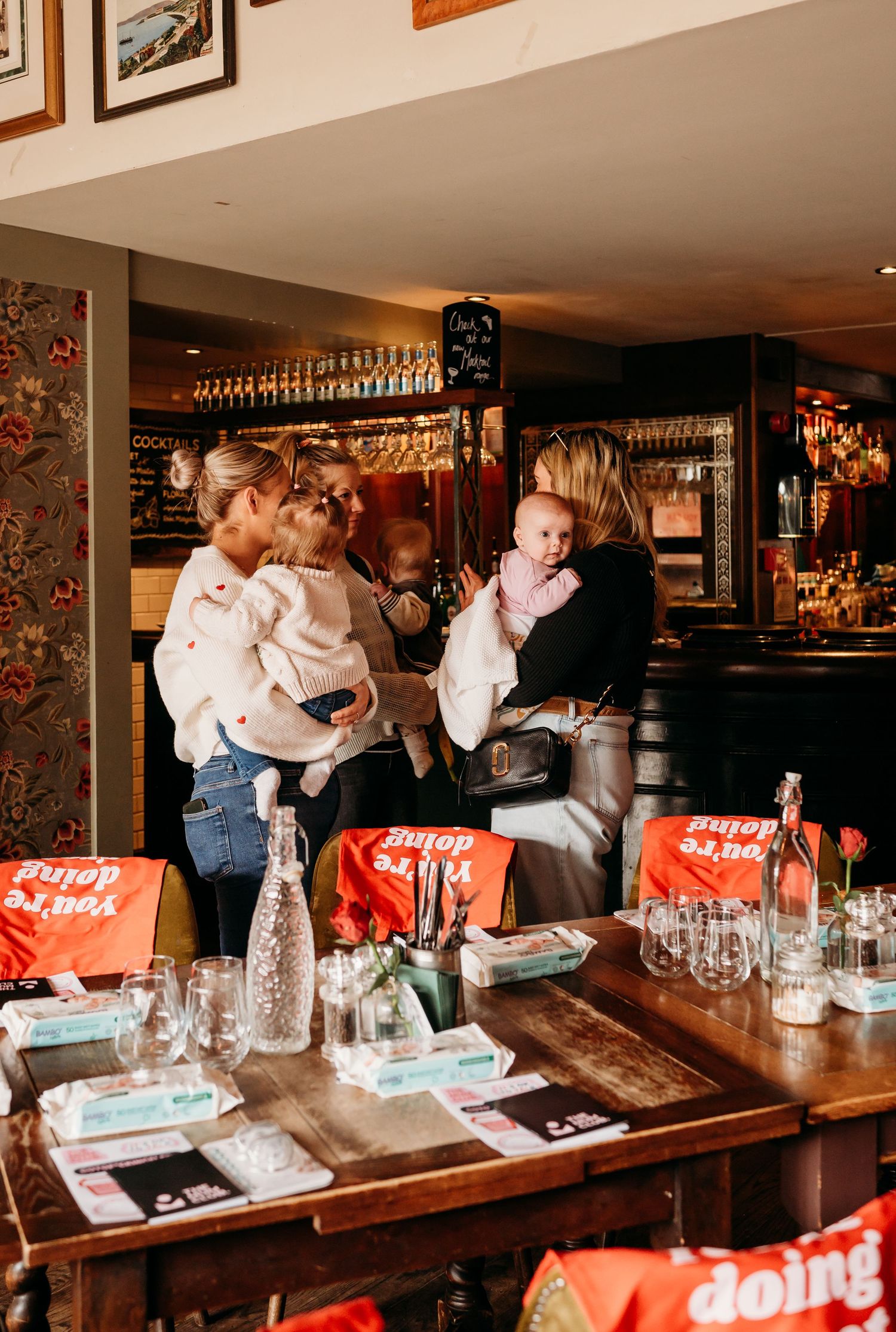 People gathering for drinks and conversation around a restaurant bar counter with red Coca-Cola branding visible on the tables.