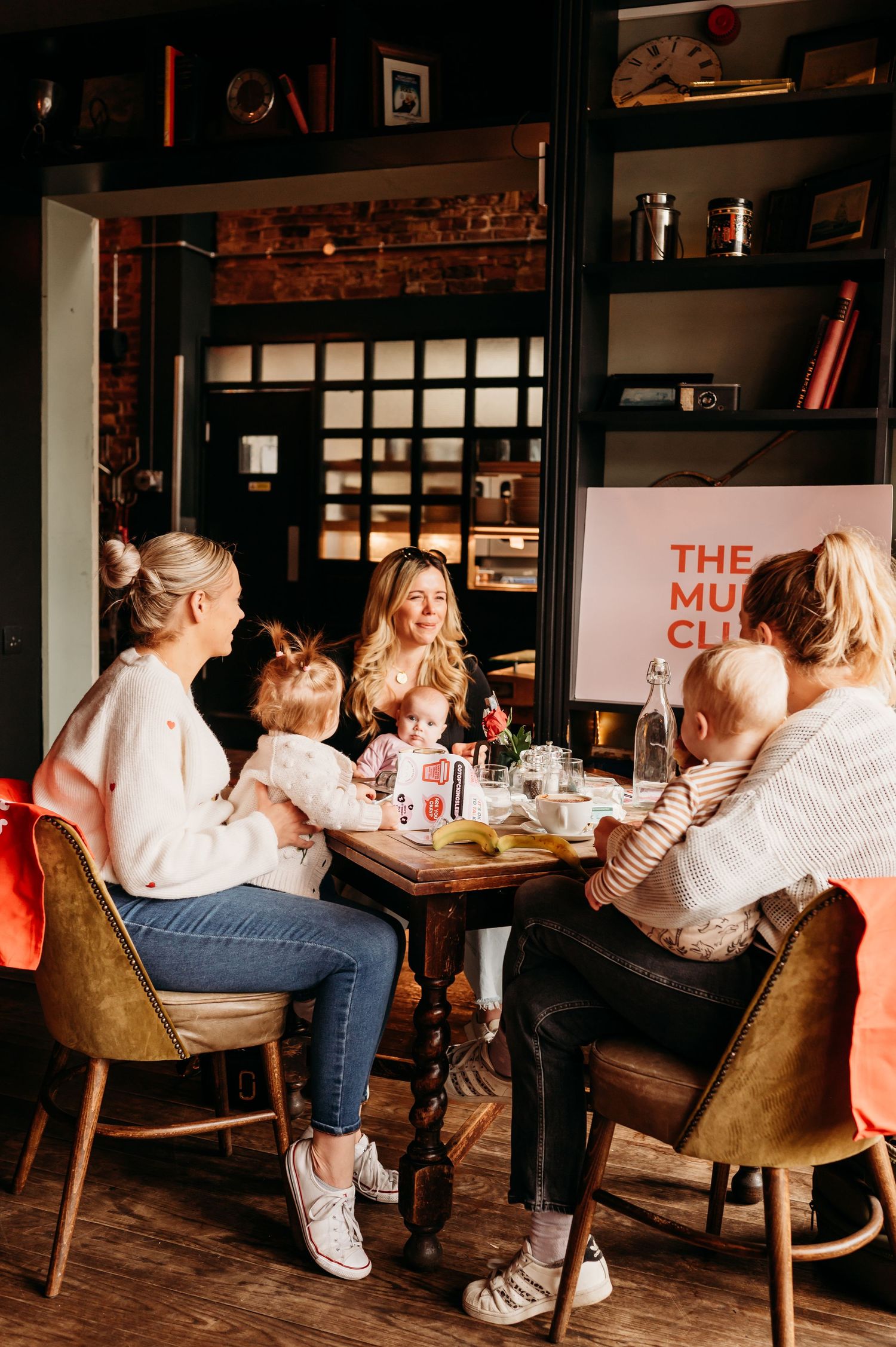 Group enjoying coffee and conversation at a cozy restaurant with wooden tables and vintage velvet chairs.