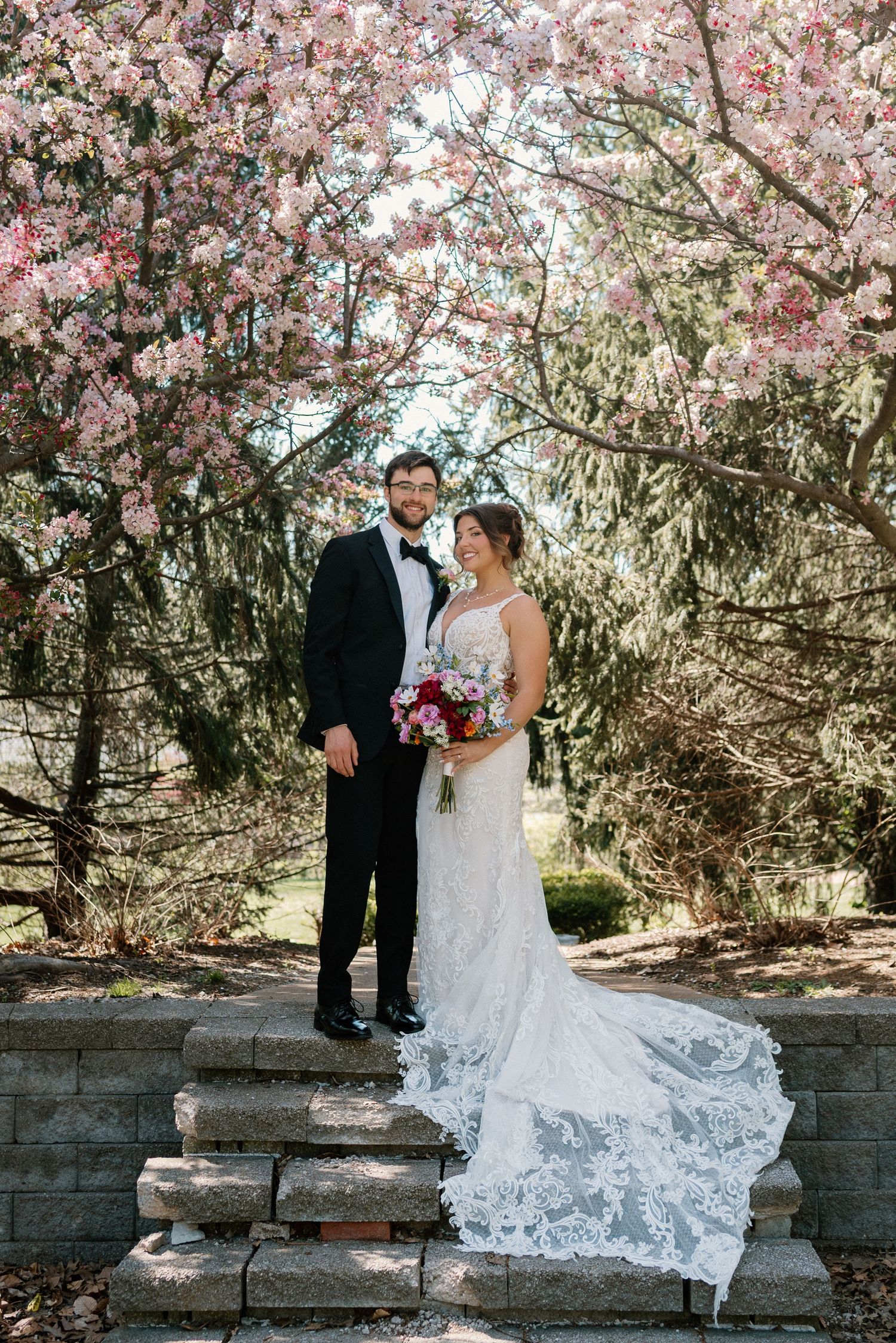 Newlyweds posing under beautiful blooming cherry blossoms with bride's lace dress trailing.