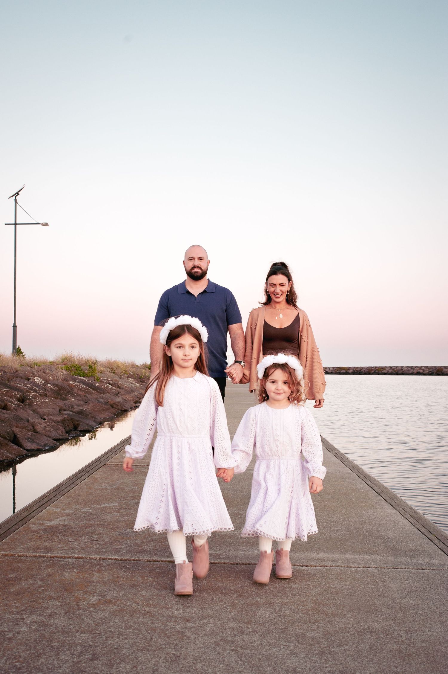 Family portrait on a coastal pier at sunset with water and sky in soft pink tones.
Altona Family Photographer Melbourne