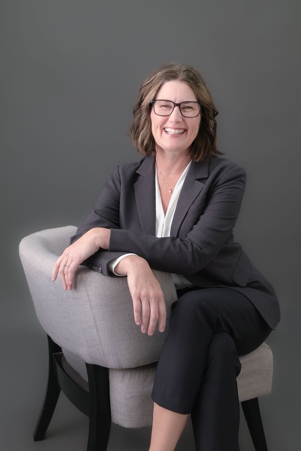 Corporate headshots showing relaxed poses in business attire on grey chair.