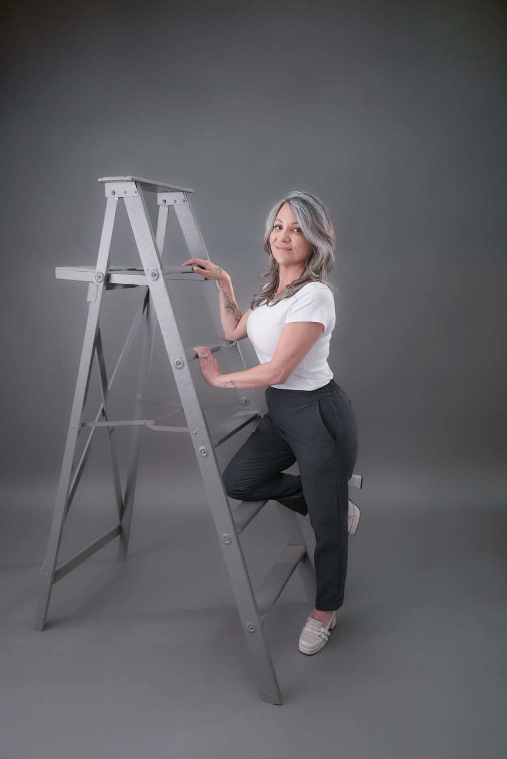Studio portraits with a wooden ladder prop against a grey background.