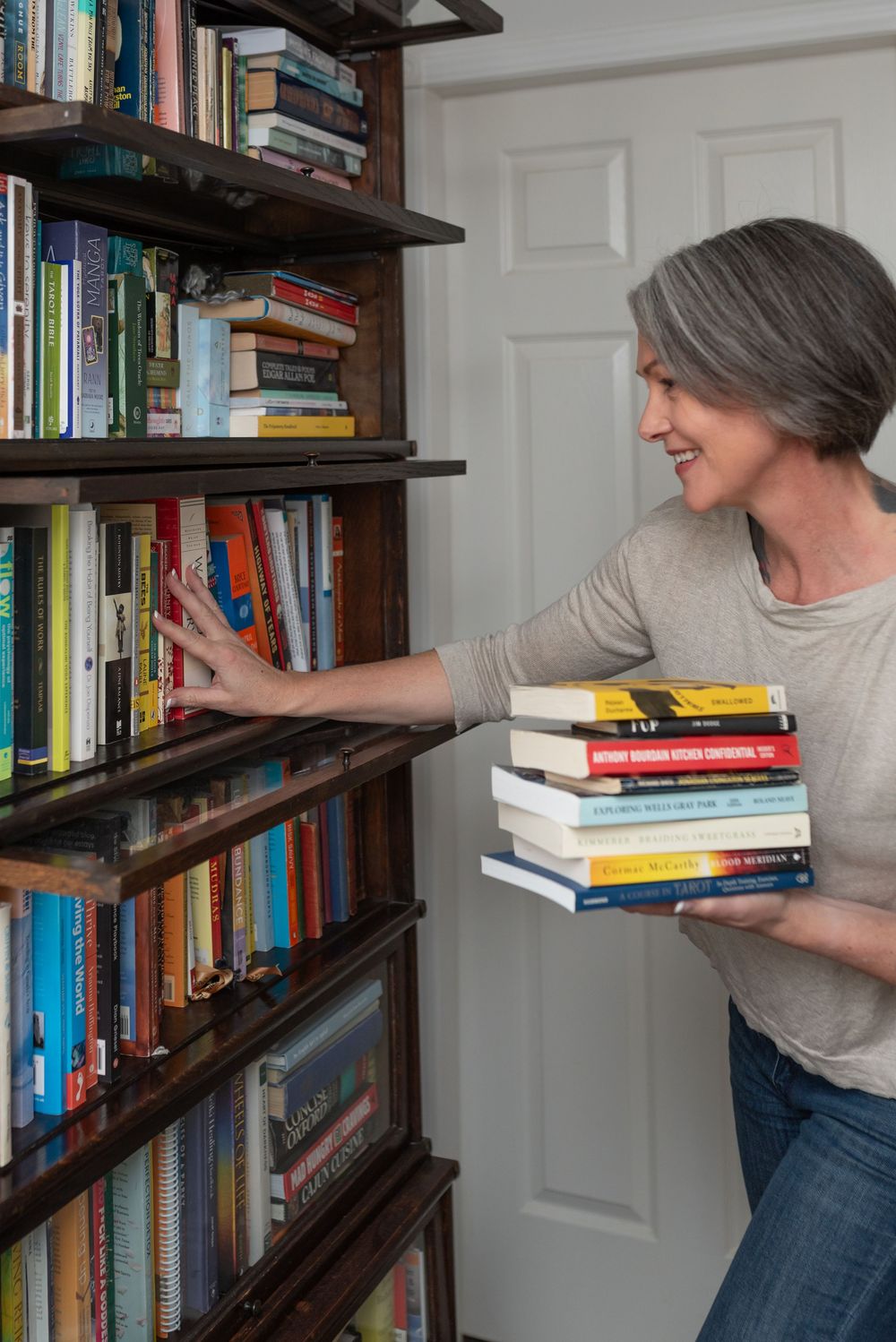Person organizing books on dark wooden floating shelves mounted on a white wall in a home library.