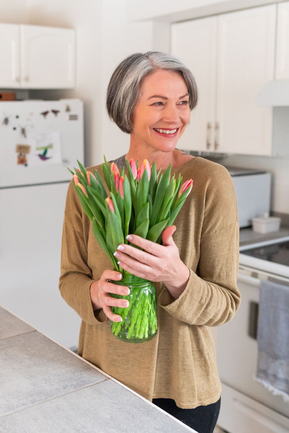 A sequence of images showing someone holding and admiring a fresh bouquet of pink and red tulips in a bright kitchen.