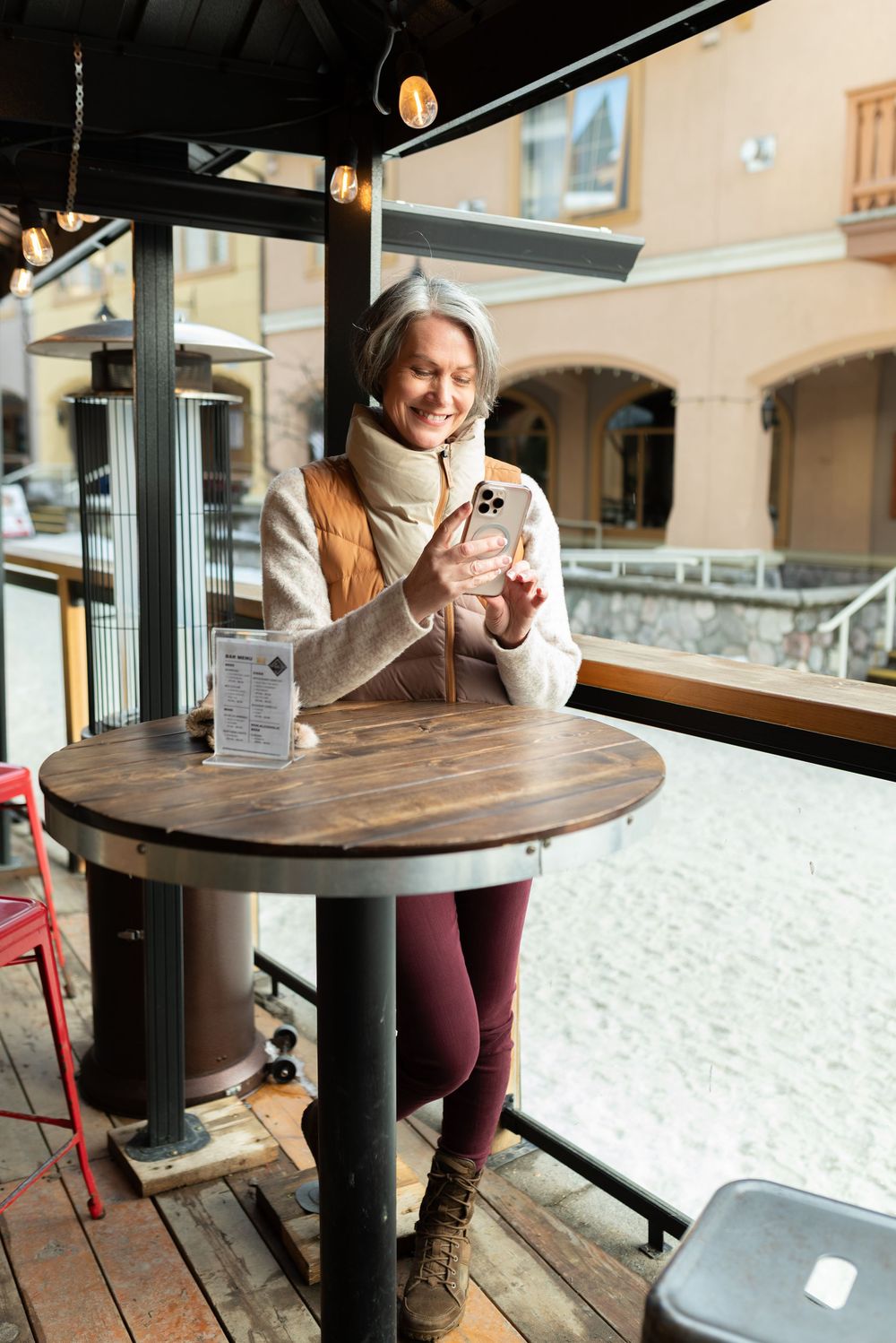 Person sitting at a round wooden table in a cozy cafe interior with large windows and warm lighting.