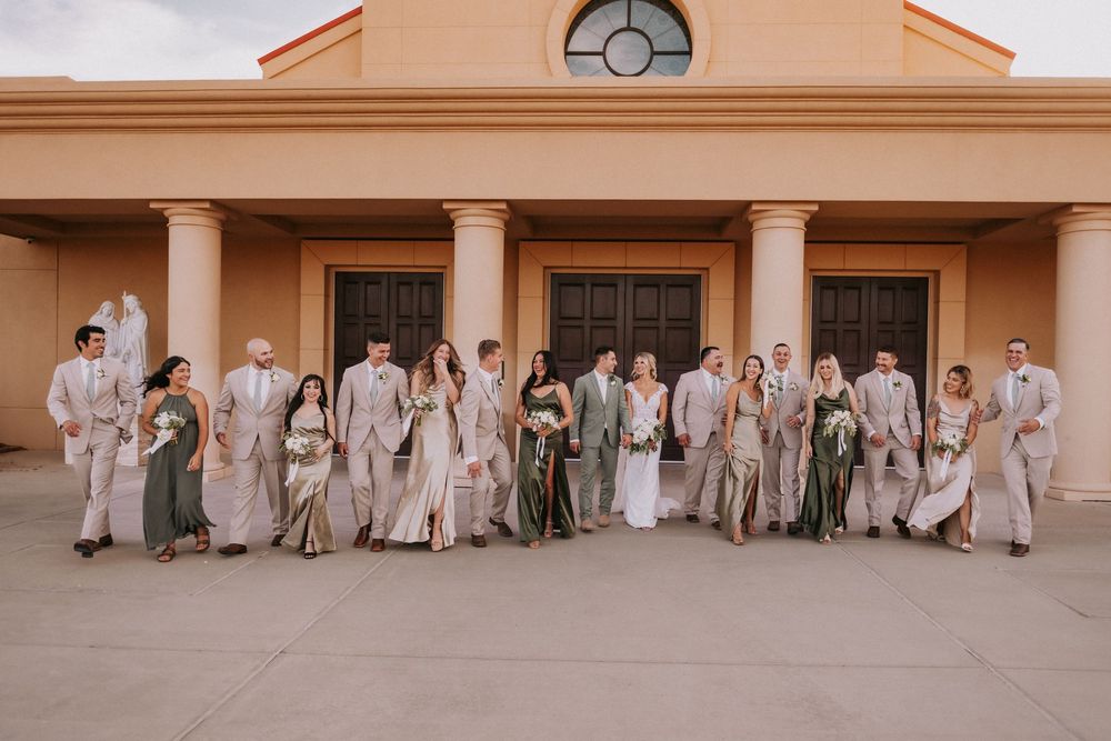 A wedding party poses in neutral attire outside a building with columns and terracotta walls. Affordable wedding photographers in New Mexico