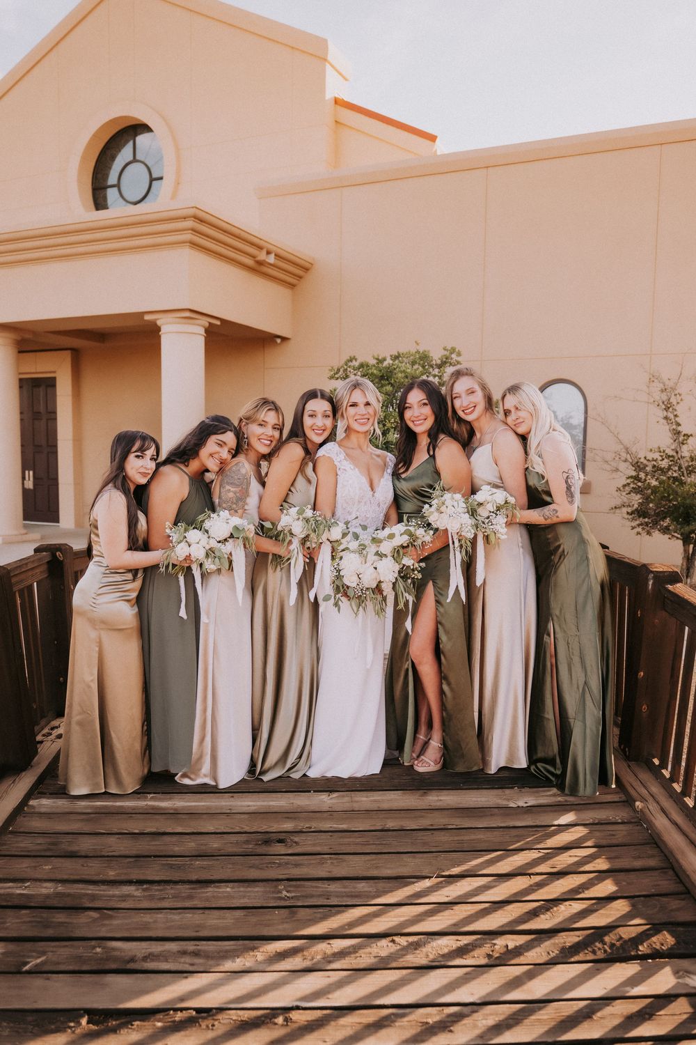 Group of bridesmaids in neutral-toned dresses pose together outside a peach-colored building. Santa Fe wedding photographer NM