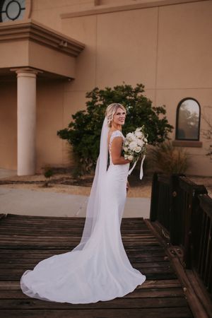 A white bridal gown with flowing train draped elegantly across a wooden deck in multiple romantic poses. Affordable wedding photographer abq