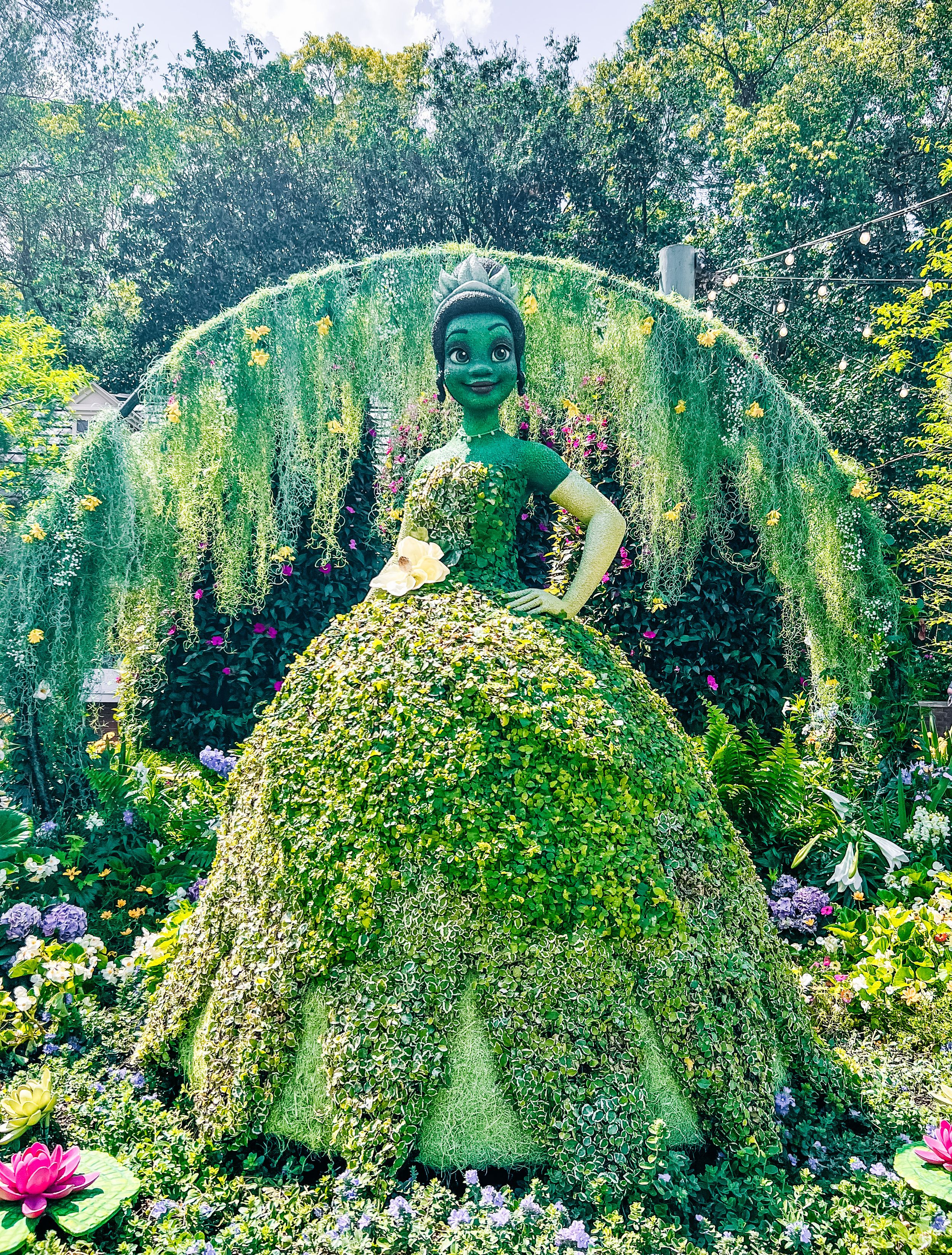 Elegant topiary figure in a flowing dress surrounded by purple flowers and hanging vines.