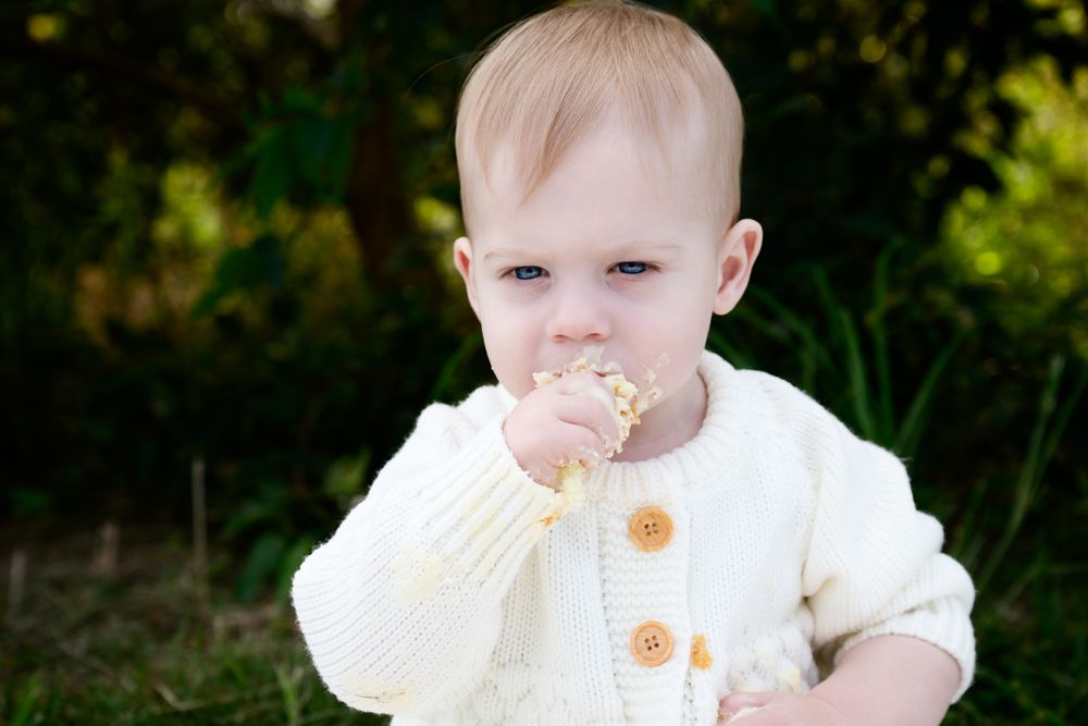 A collection of images showing a small baby in a cream-colored dress playing outdoors in natural lighting.