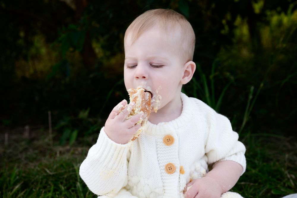 A small child sits outdoors in natural lighting enjoying a tasty pastry or baked treat.