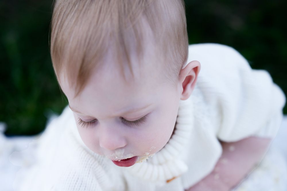 Close-up view of a baby in a white sweater looking downward in a pensive moment.