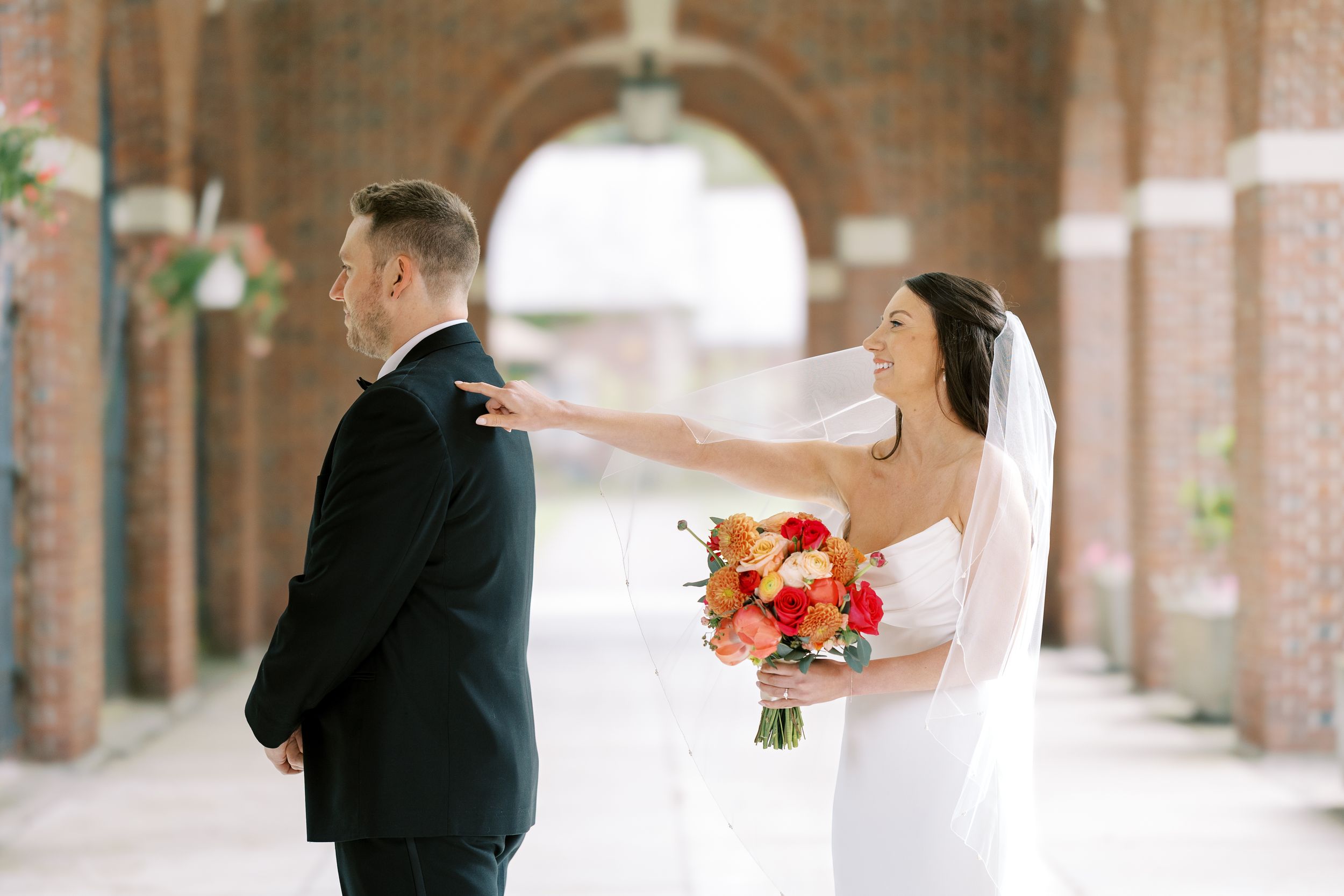 Couple sharing a tender first look moment in a brick-lined covered walkway at their wedding.