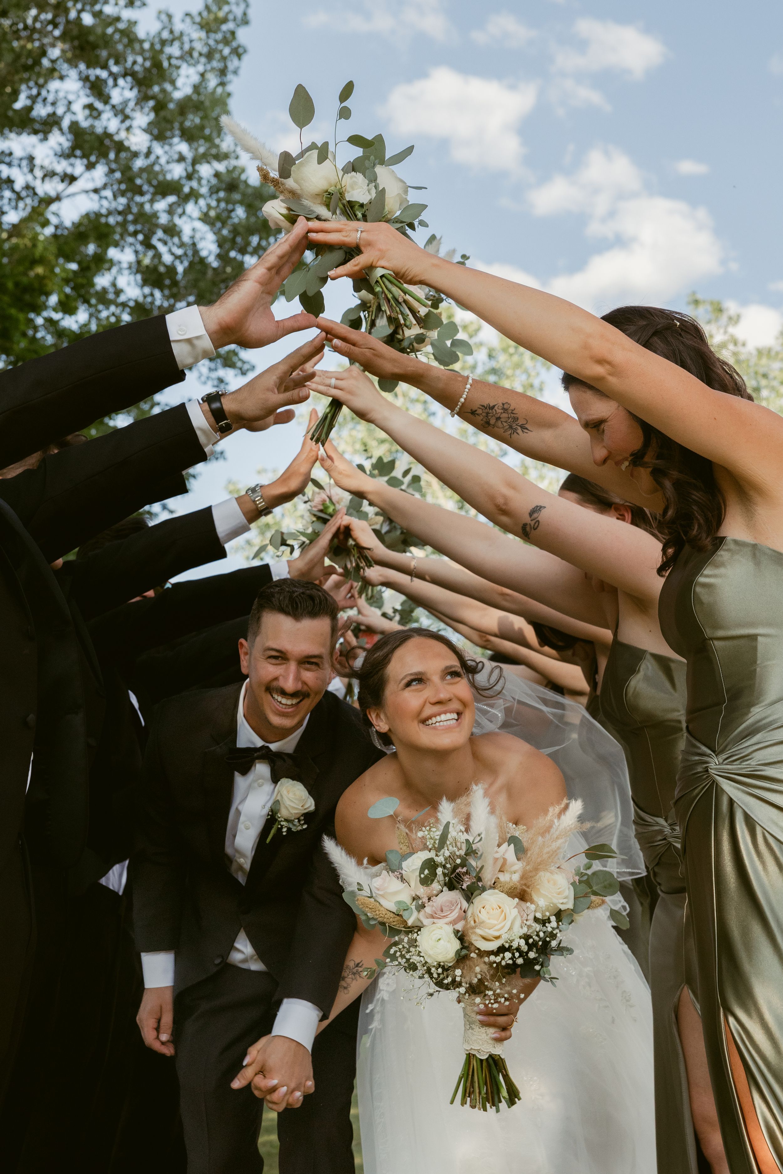 Wedding party raises their arms in celebration as newlyweds walk beneath them.