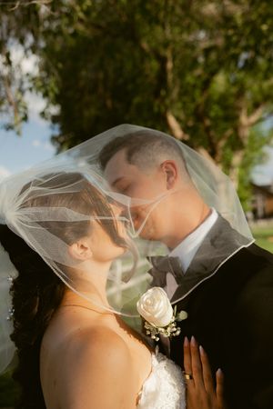 A romantic wedding moment captured through a delicate veil in natural outdoor lighting.