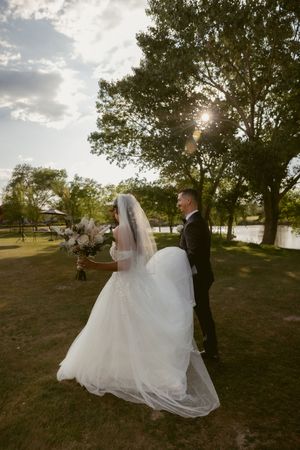 Wedding couple poses in a scenic outdoor setting with trees and sunlight.