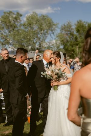 Wedding ceremony guests gather outdoors under trees during a late afternoon celebration.