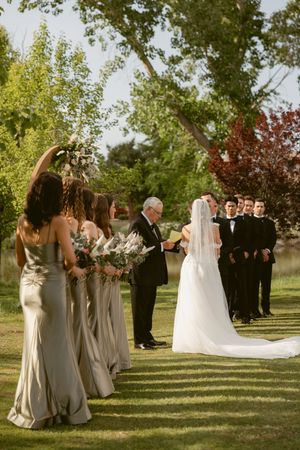 Wedding party in formal attire stands on manicured lawn during golden hour.